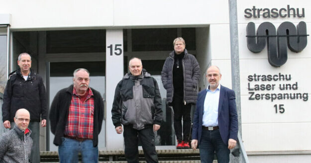 2024_02_Beitragsbild_LUZ Team_955x500 Die Mitarbeiter der straschu Laser- und Zerspanungs- GmbH stehen auf einer Treppe vor dem Gebäude des Unternehmens und lächeln in die Kamera.