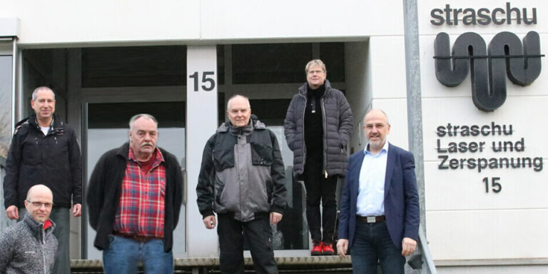 2024_02_Beitragsbild_LUZ Team_955x500 Die Mitarbeiter der straschu Laser- und Zerspanungs- GmbH stehen auf einer Treppe vor dem Gebäude des Unternehmens und lächeln in die Kamera.