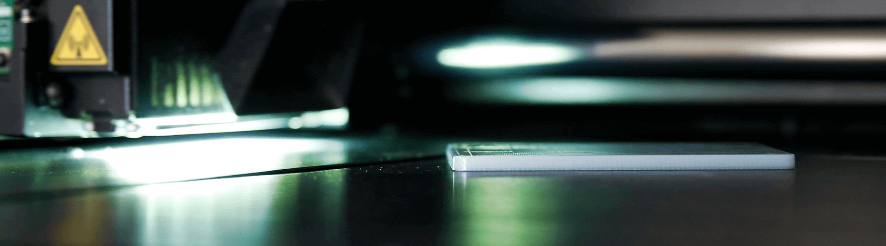 Auf einer dunklen Oberfläche liegt eine metallene Platte und im Hintergrund auf der linken Seite ist eine Maschine.