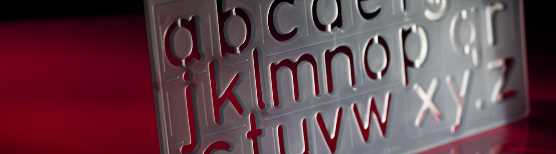 Eine Musterschablone mit ausgefrästen Buchstaben in Reihenfolge des Alphabets vor rotem Hintergrund