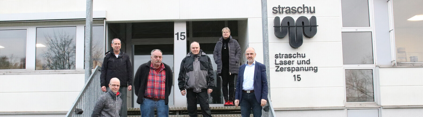 Die Mitarbeiter der straschu Laser- und Zerspanungs- GmbH stehen auf einer Treppe vor dem Gebäude des Unternehmens und lächeln in die Kamera.